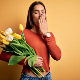 Der biologische Jetlag: Warum der März uns oft müder macht als der Januar Gähnende Frau mit Frühjahrsblumen in der Hand als Symbol für Frühjahrsmüdigkeit