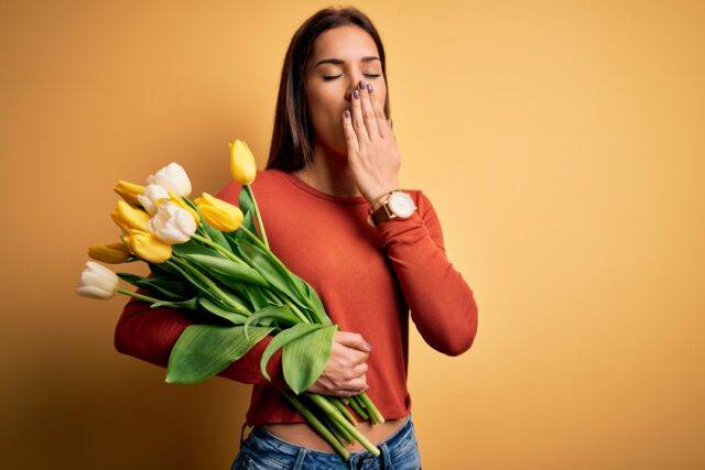 Gähnende Frau mit Frühjahrsblumen in der Hand als Symbol für Frühjahrsmüdigkeit